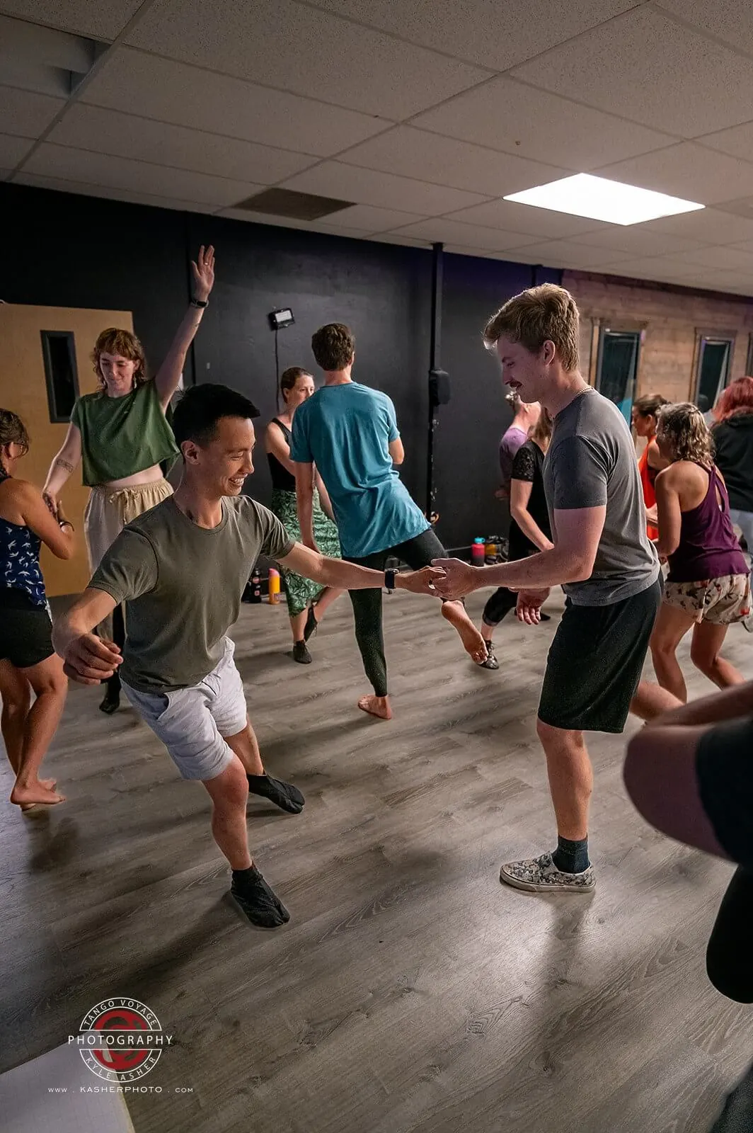 Two dancers mid-move, laughing, surrounded by other dancers on the floor